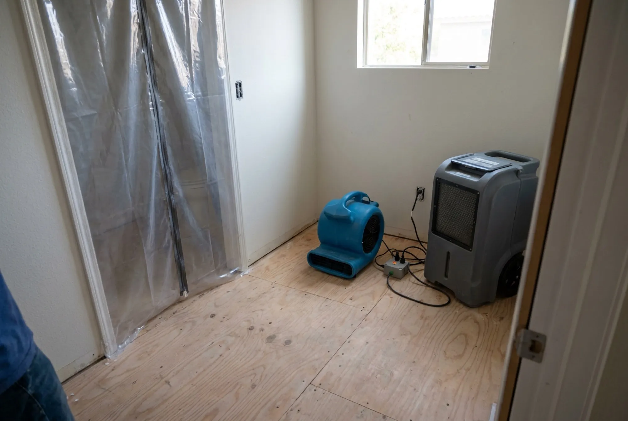 A Phoenix bathroom stripped to the subfloor and sanitized after sewage cleanup, with drying equipment running and containment barriers still in place.