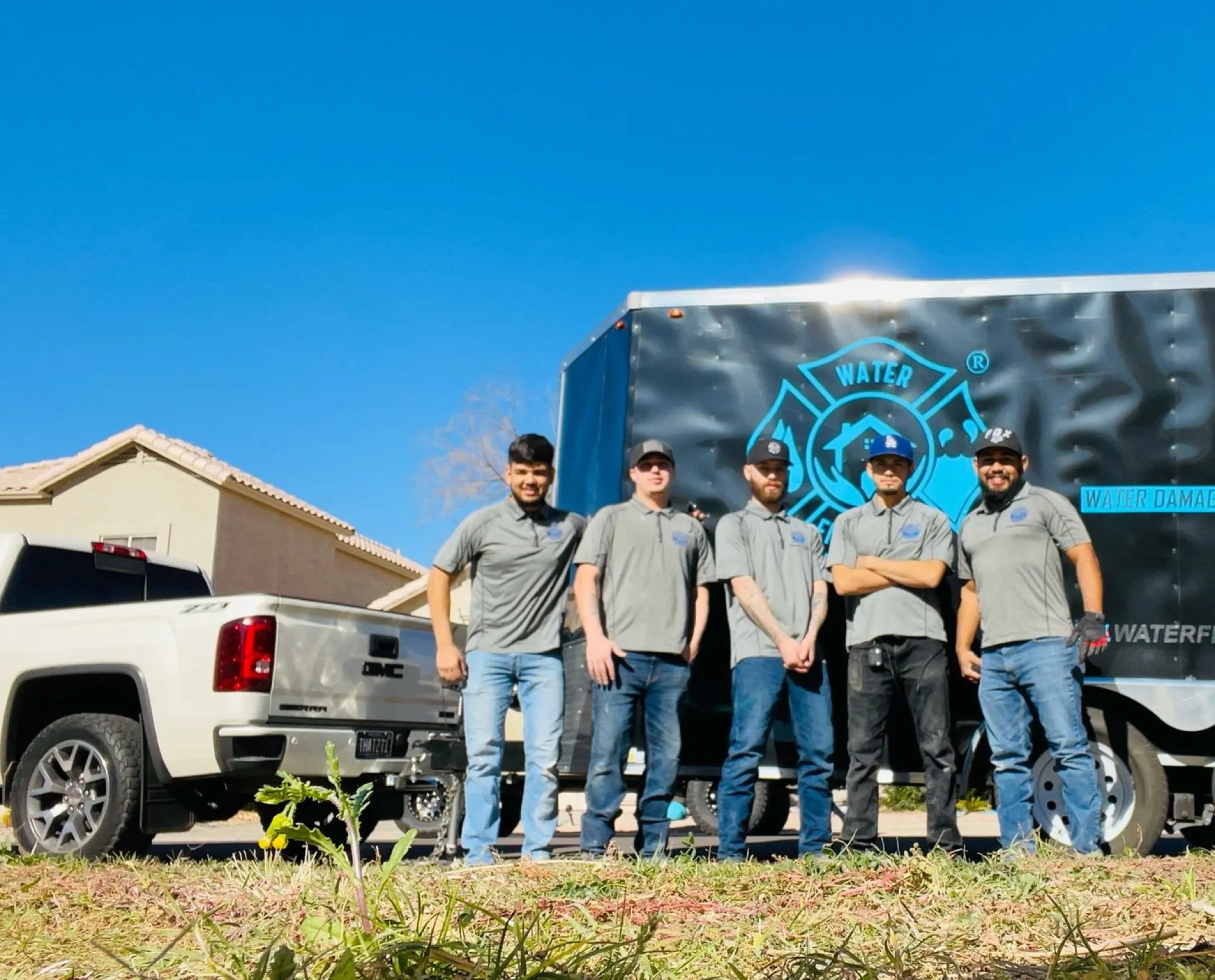 The Water Fighters crew stands together in front of their service trucks on a Phoenix job site in the early morning.